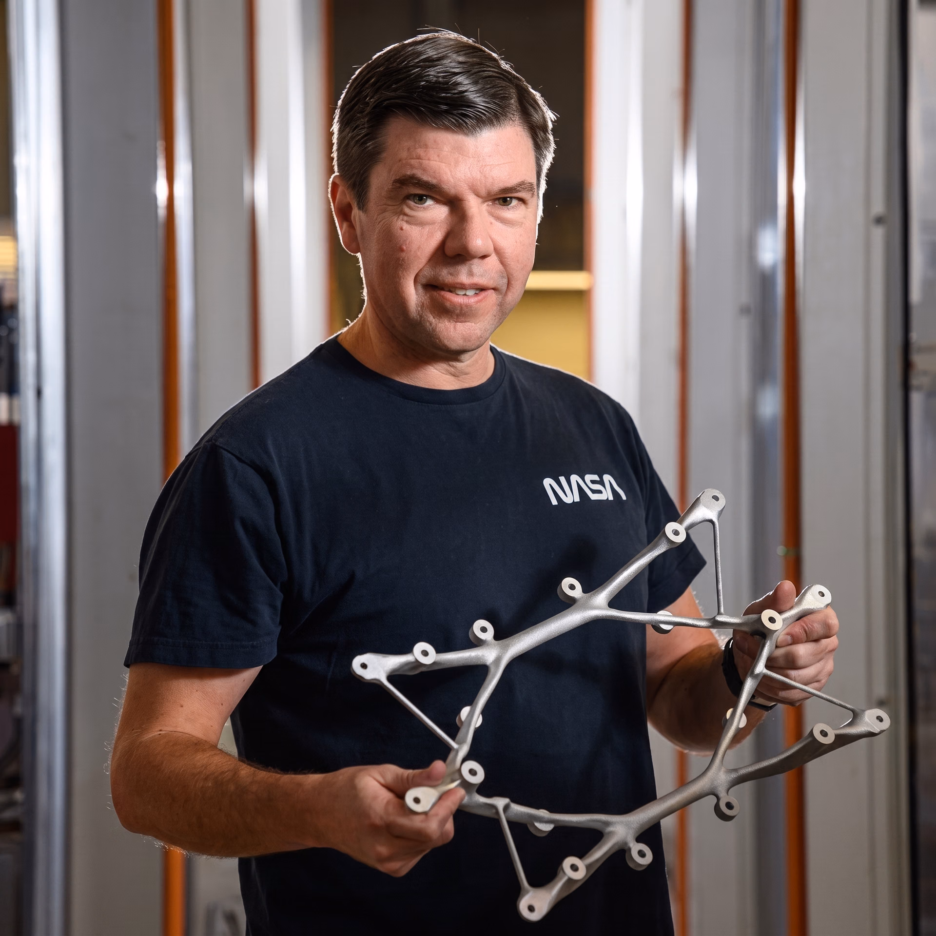 NASA Research Engineer Ryan McClelland holding a 3D-printed titanium structural mount designed with generative AI
