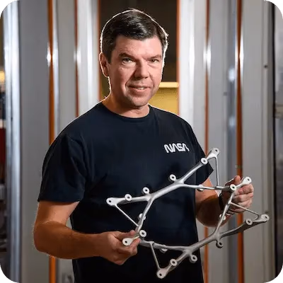 생성형 AI로 설계되어 3D 프린팅된 티타늄 구조 마운트를 들고 있는 NASA 연구 엔지니어 Ryan McClelland